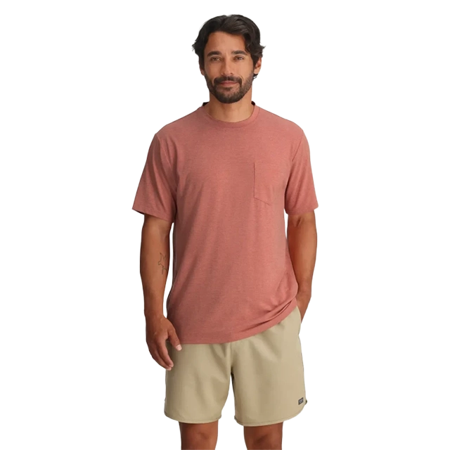 Man wearing a red shirt and beige shorts, standing and smiling.