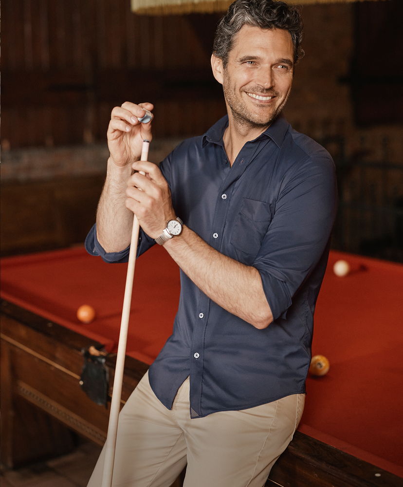 Smiling man holding a pool cue beside a billiards table.