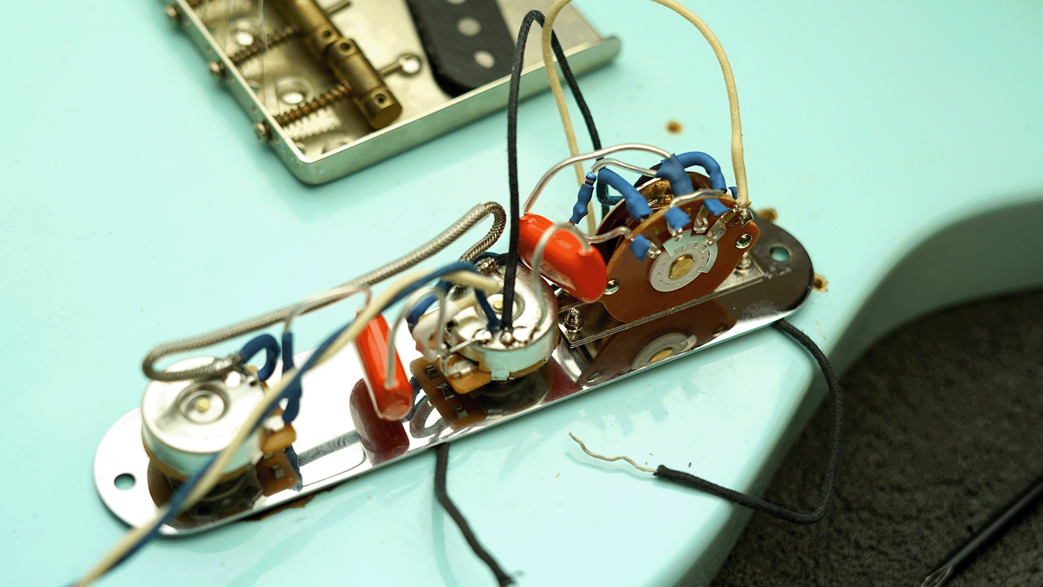Guitar wiring with components and connections on a turquoise surface.
