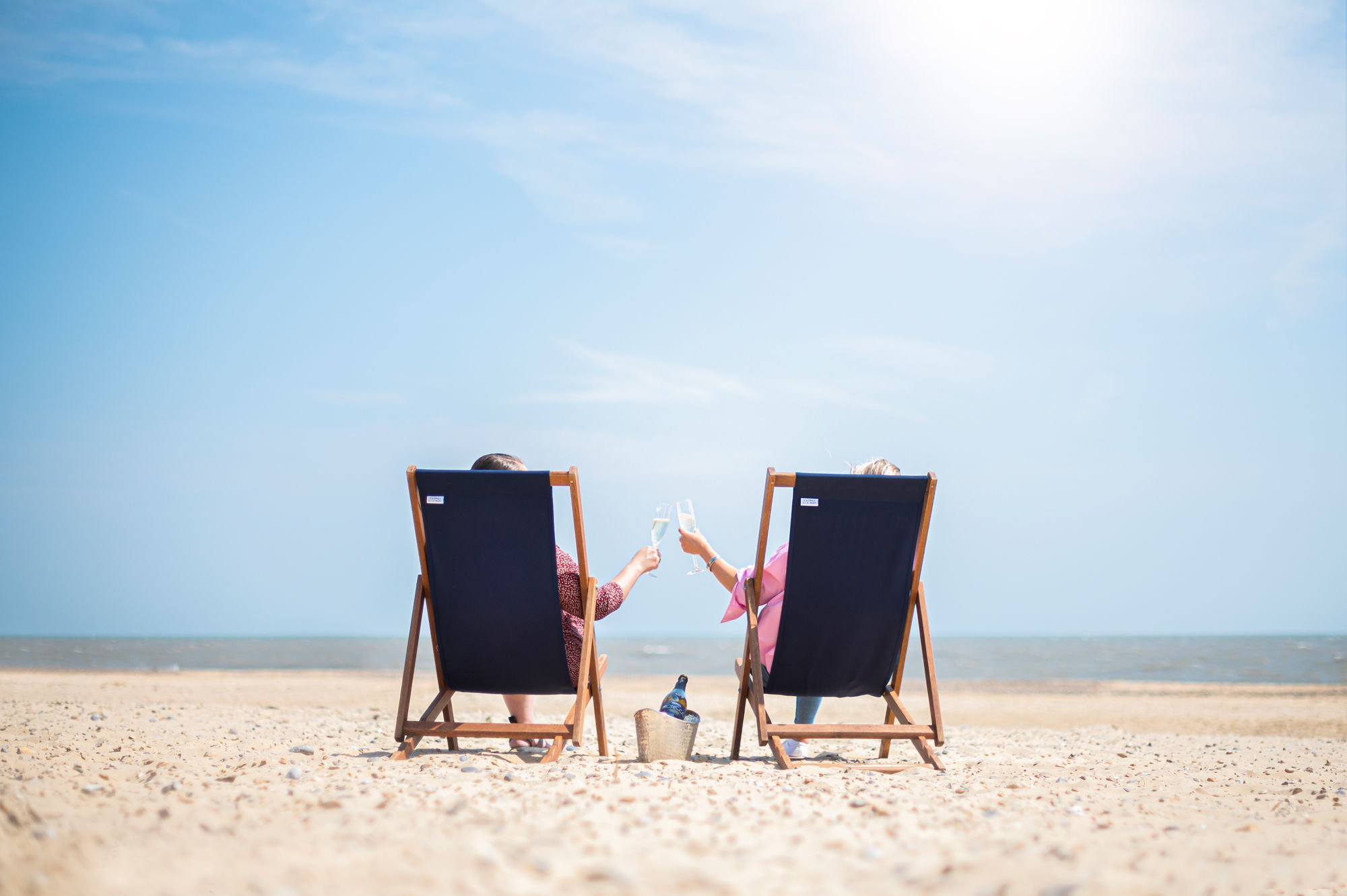 Two people relaxing in beach chairs, holding hands by the ocean.