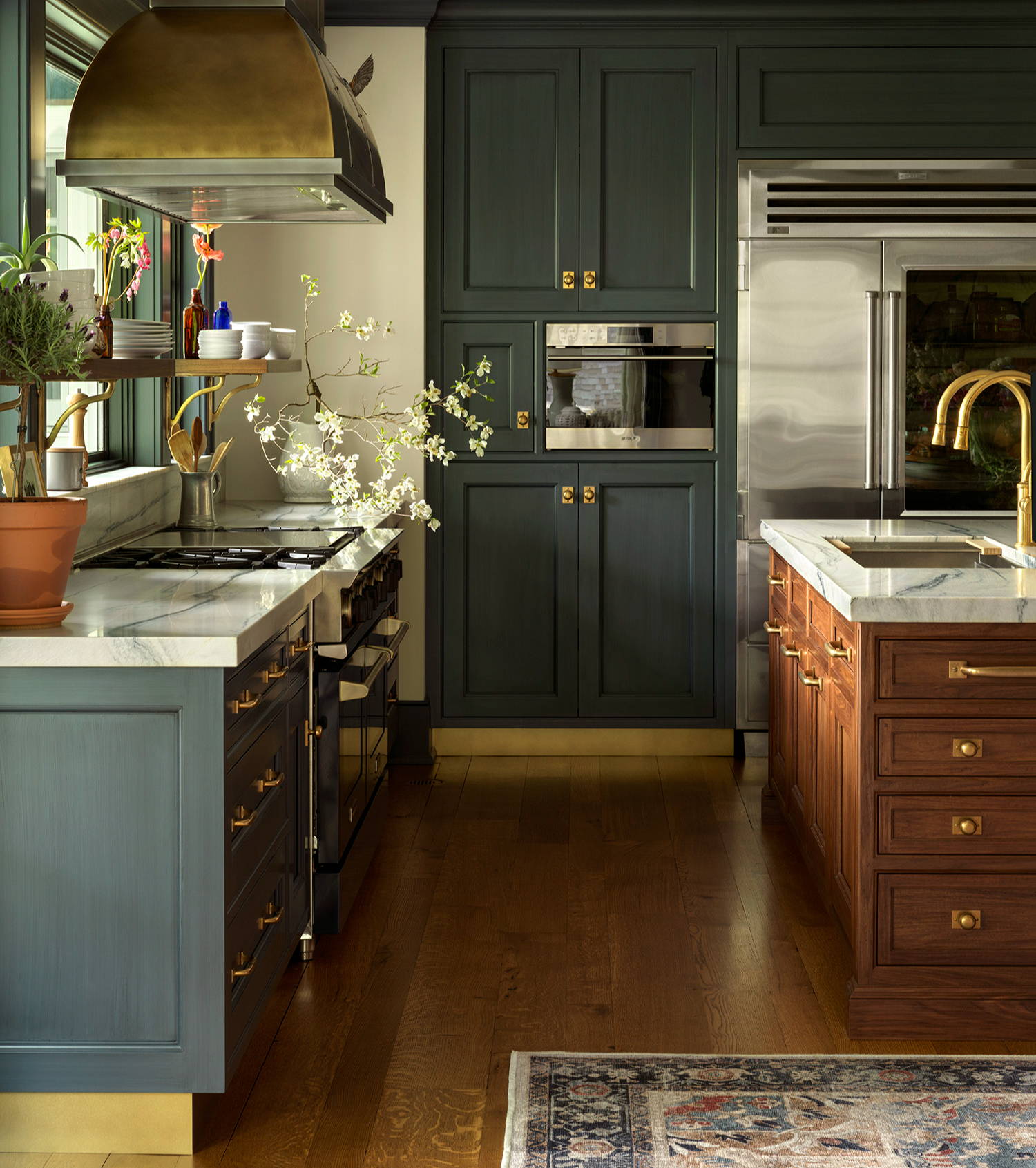 Wood and navy kitchen with brass cabinet hardware, wood flooring and marble worktops