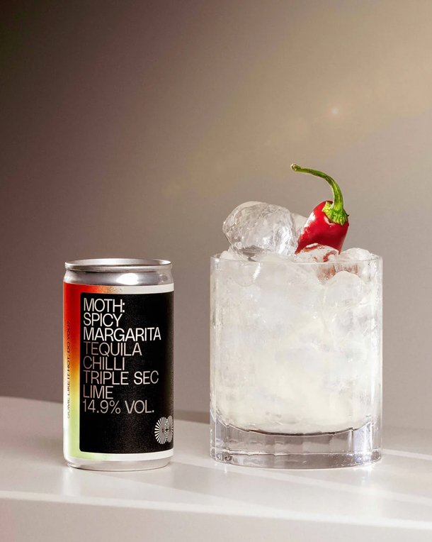 Can of margarita next to a glass with ice and a cherry on top.