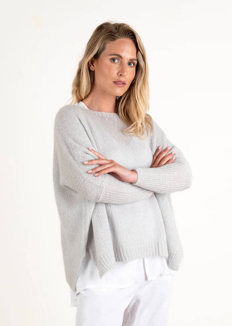 A model wearing a light grey knitted sweater over a white top, white trousers and off white chunky slides
