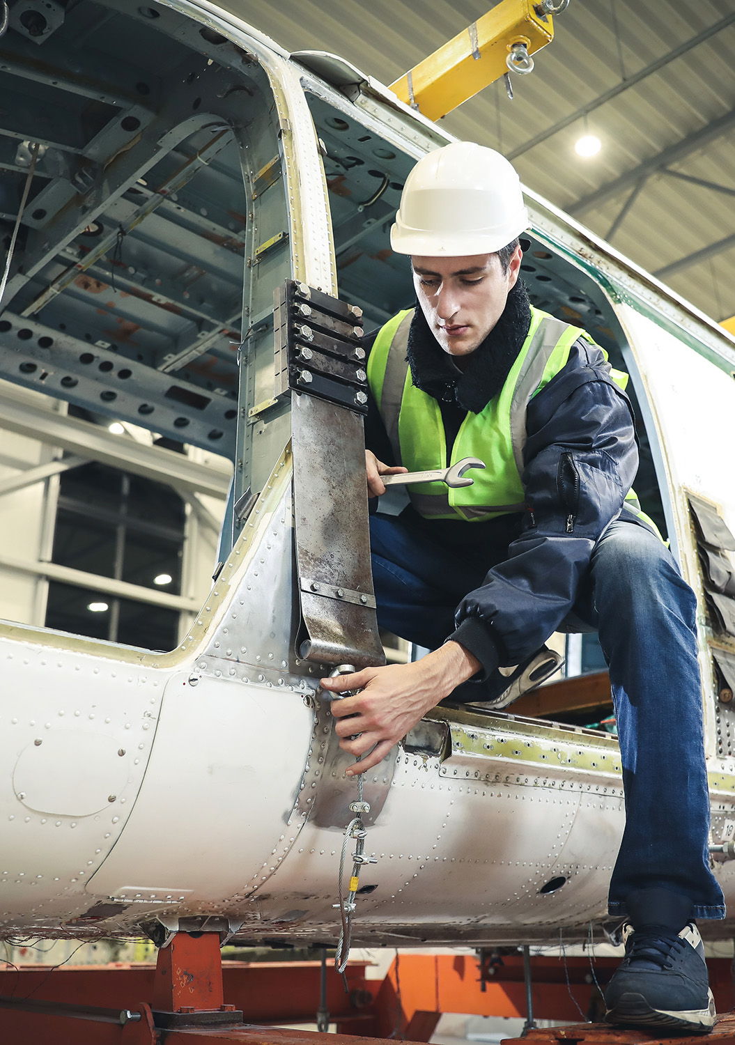 A technician in a hard hat repairs an aircraft fuselage.