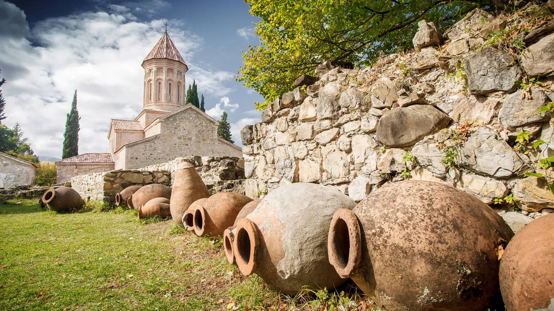Qvevri wine pots in the Alazani Valley, with a medieval Orthodox church and the Caucasus Mountains in the distance, reflecting Georgia's winemaking heritage.