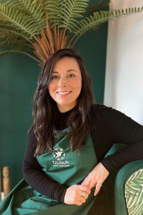 A smiling woman wearing a green apron, seated among plants.