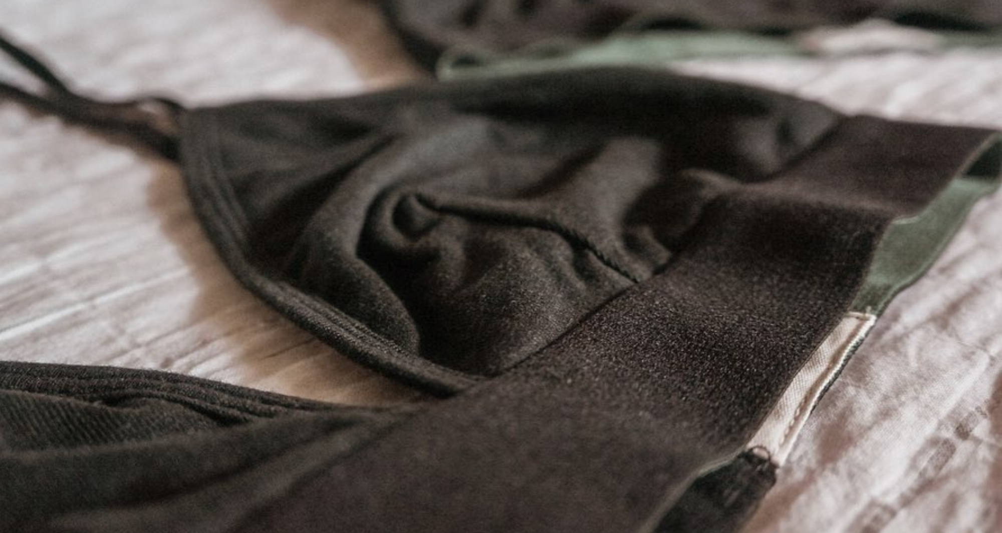 A black hemp triangle bralette, lies flat on a wrinkled linen cloth.