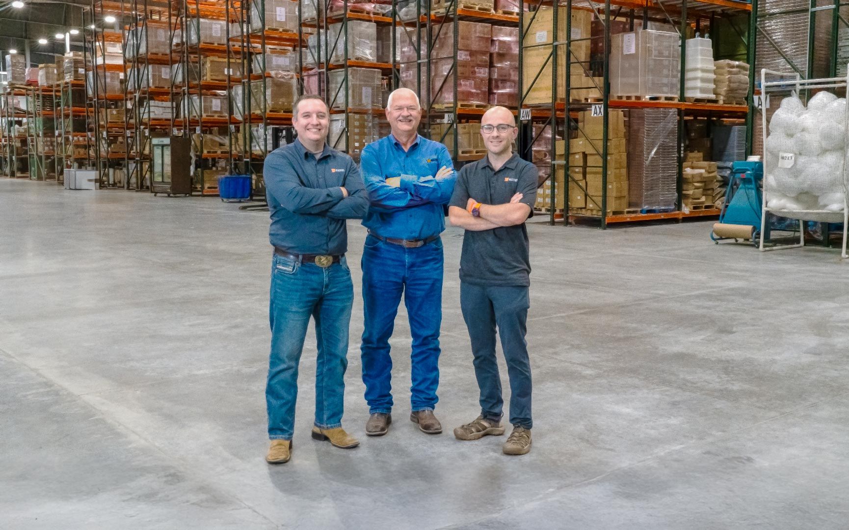 Waltons standing in a large warehouse with shelves of goods.