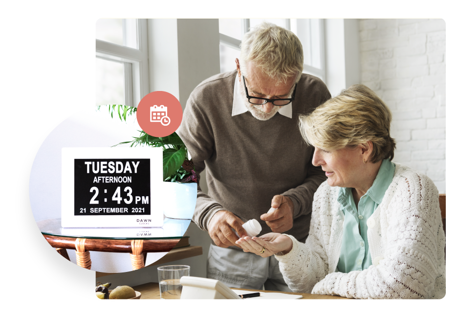 Husband handing his wife who lives with Alzheimer's and Dementia her medications. A Dawn Clock showing the day, date and time is on a table shown inset.