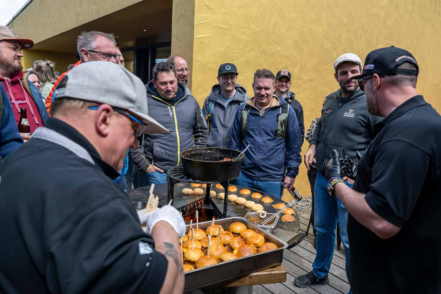 Group of people watching food being prepared outdoors.