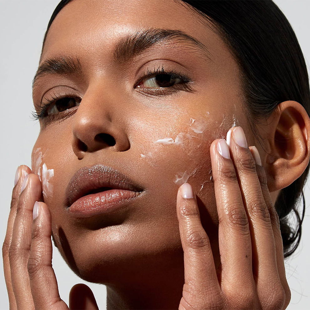 A woman applying skincare product to her face.