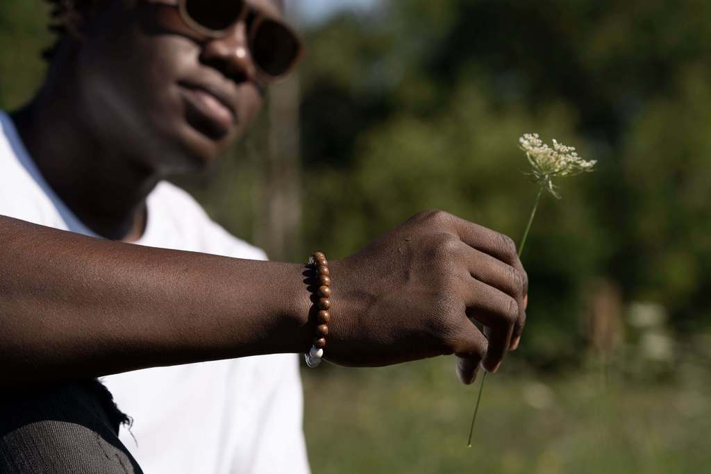 Man wearing wood bead bracelet holding a wildflower