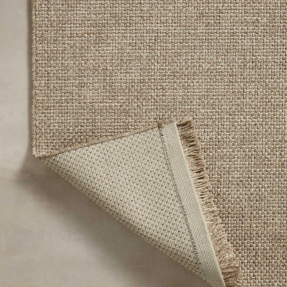 Close-up of a woven polypropylene neutral outdoor rug with durable textured weave and finished edge, highlighting weather-resistant construction for desert climates. 