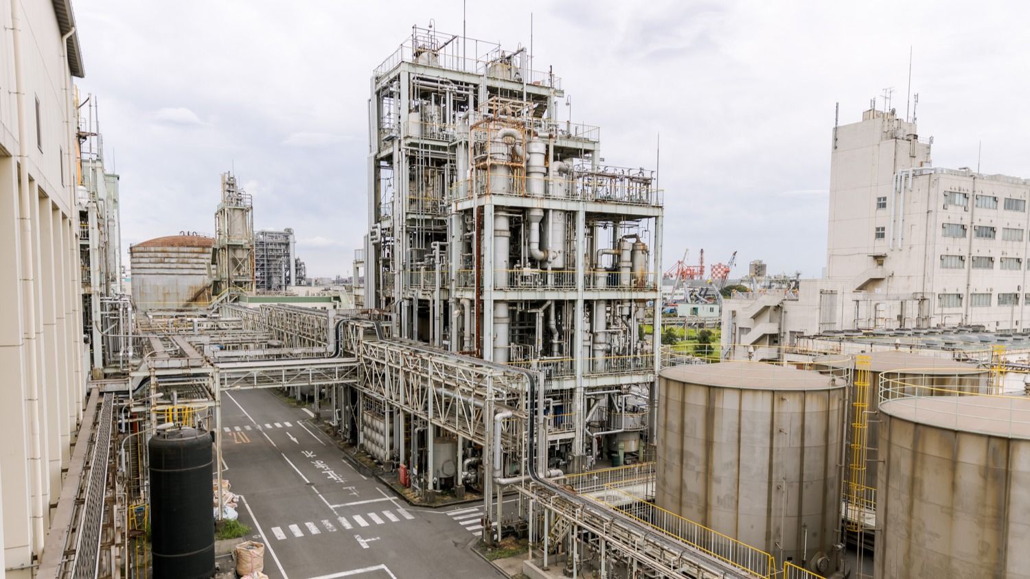 Industrial facility with large storage tanks and processing structures under a cloudy sky.