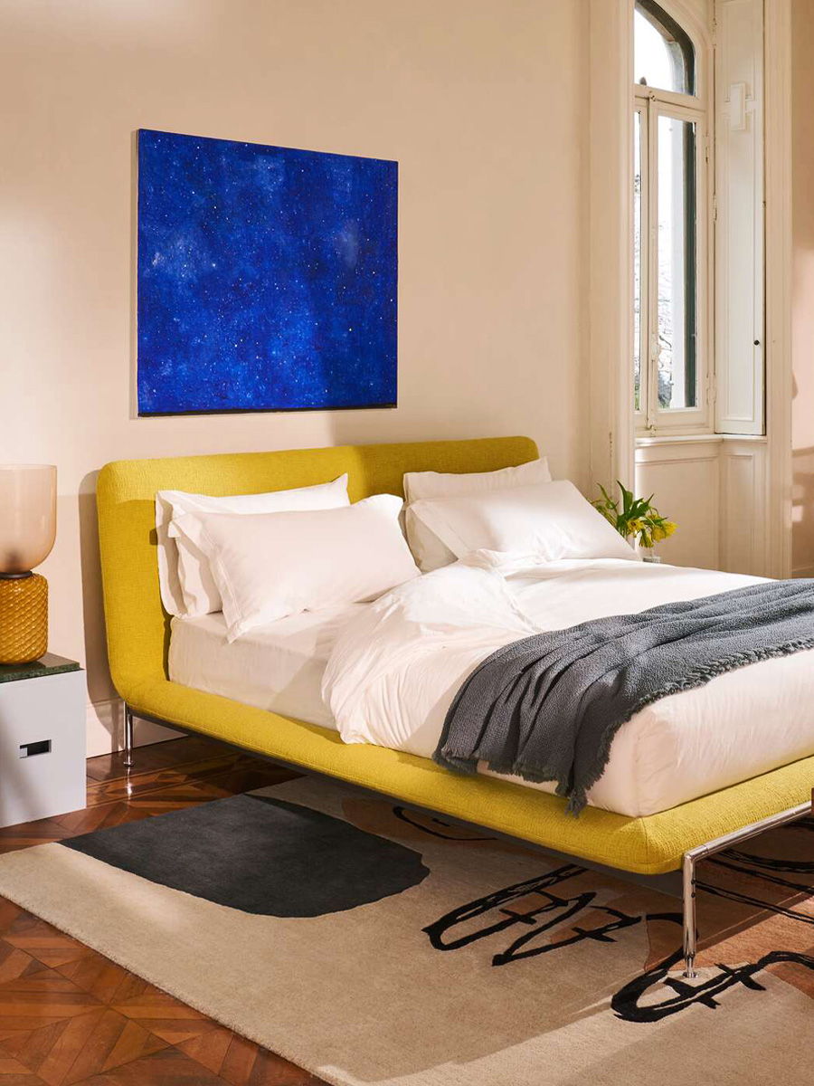 Modern bedroom with a yellow Esosoft bed by Cassina, white linens, and blue wall art.