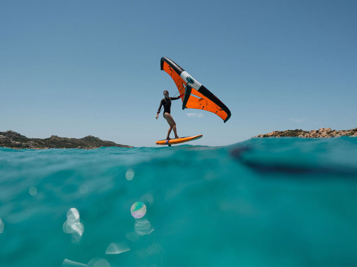 Person kitesurfing on a clear blue ocean with mountains in the background.