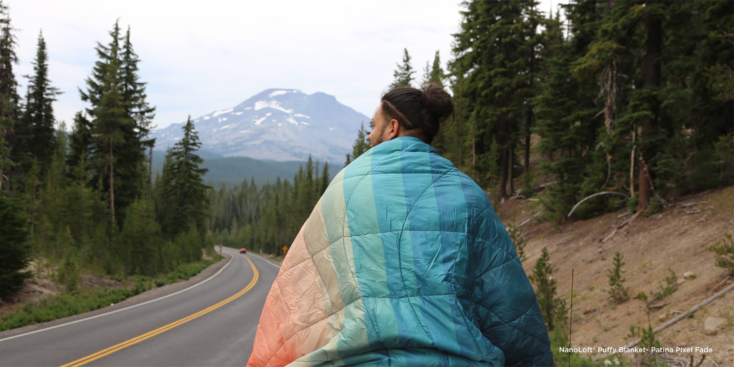 Teen wrapped in Nanoloft Puffy Blanket overlooking forestscape