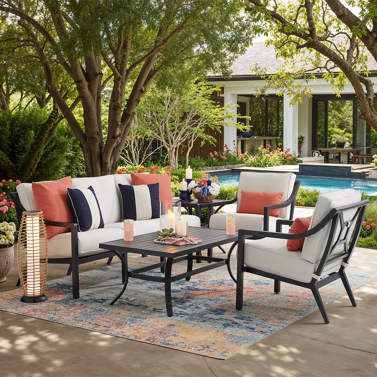 Outdoor seating area with cushions, table, and decorative elements by a pool.