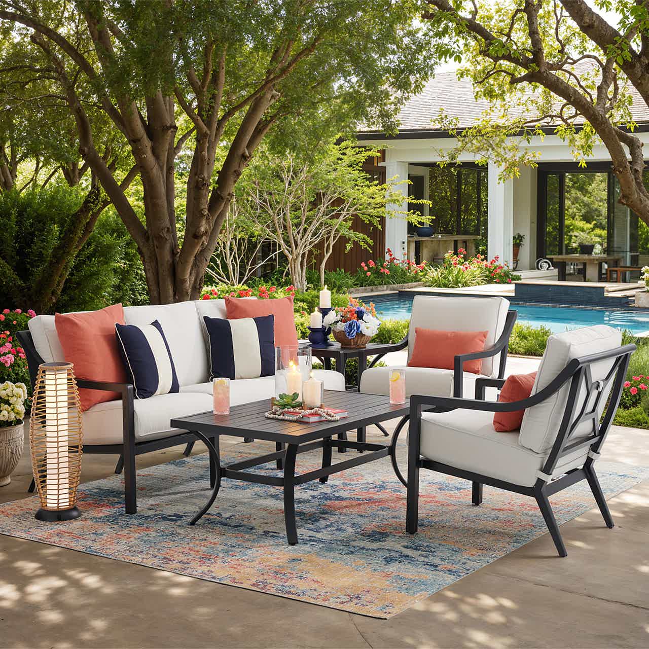 Outdoor seating area with cushions, table, and decorative elements by a pool.