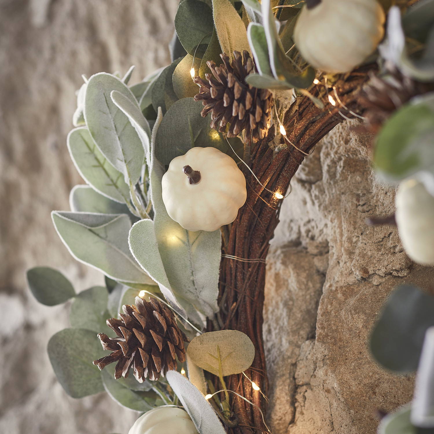 A eucalyptus and pine pumpkin wreath close up entwined with warm white micro lights.