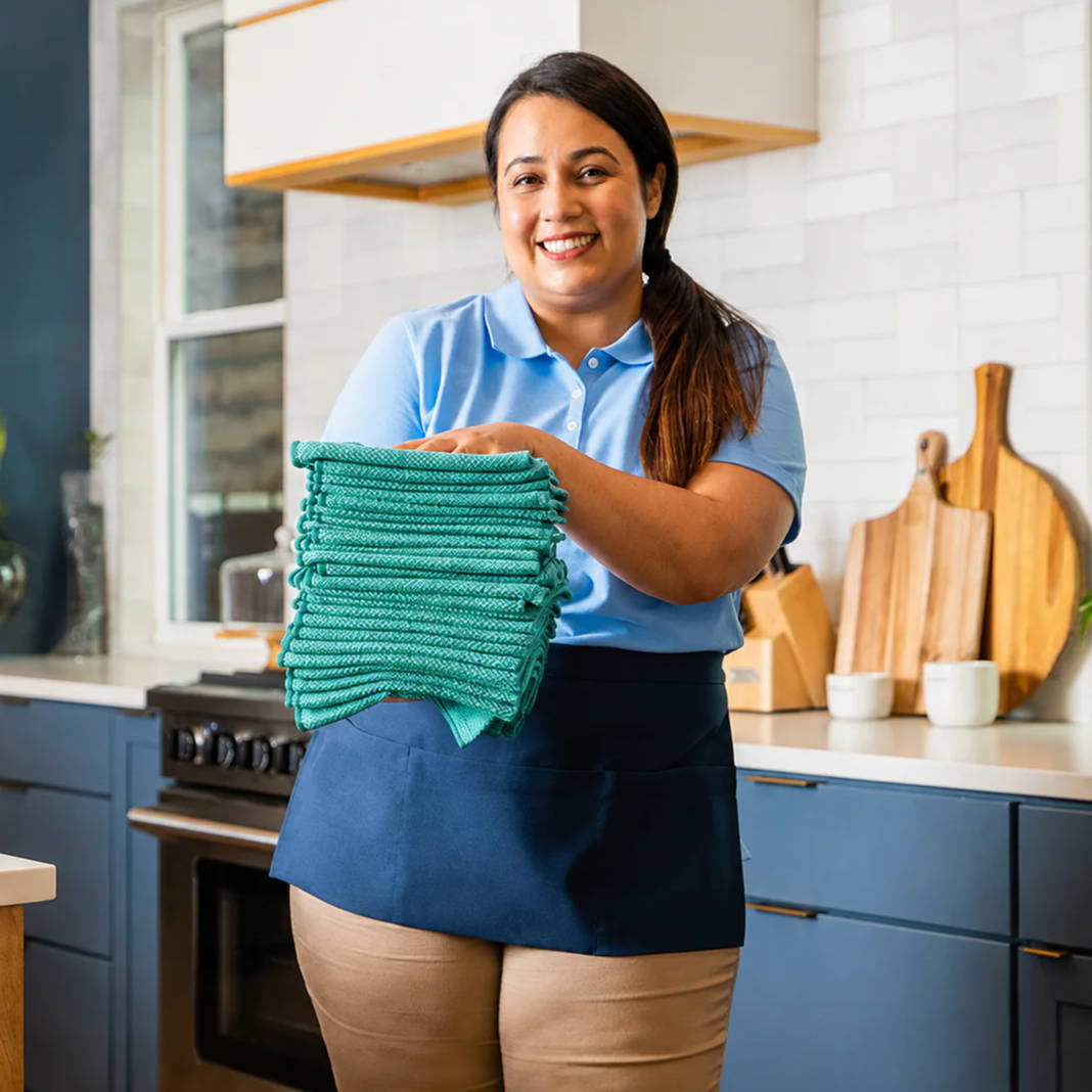 Woman in a kitchen holding folded green towels, smiling at the camera.