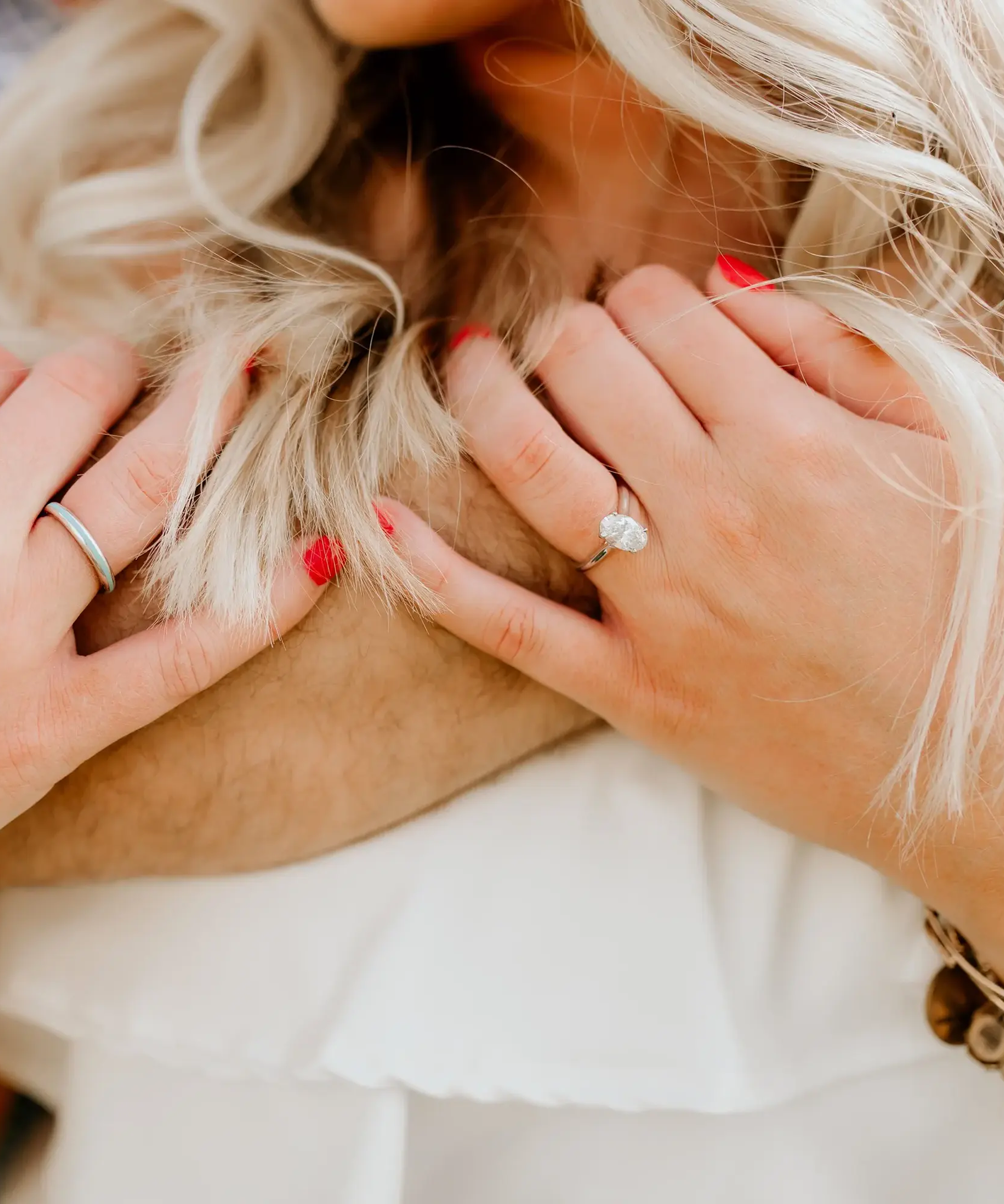 Woman's hands with rings, holding hair, wearing a white top.