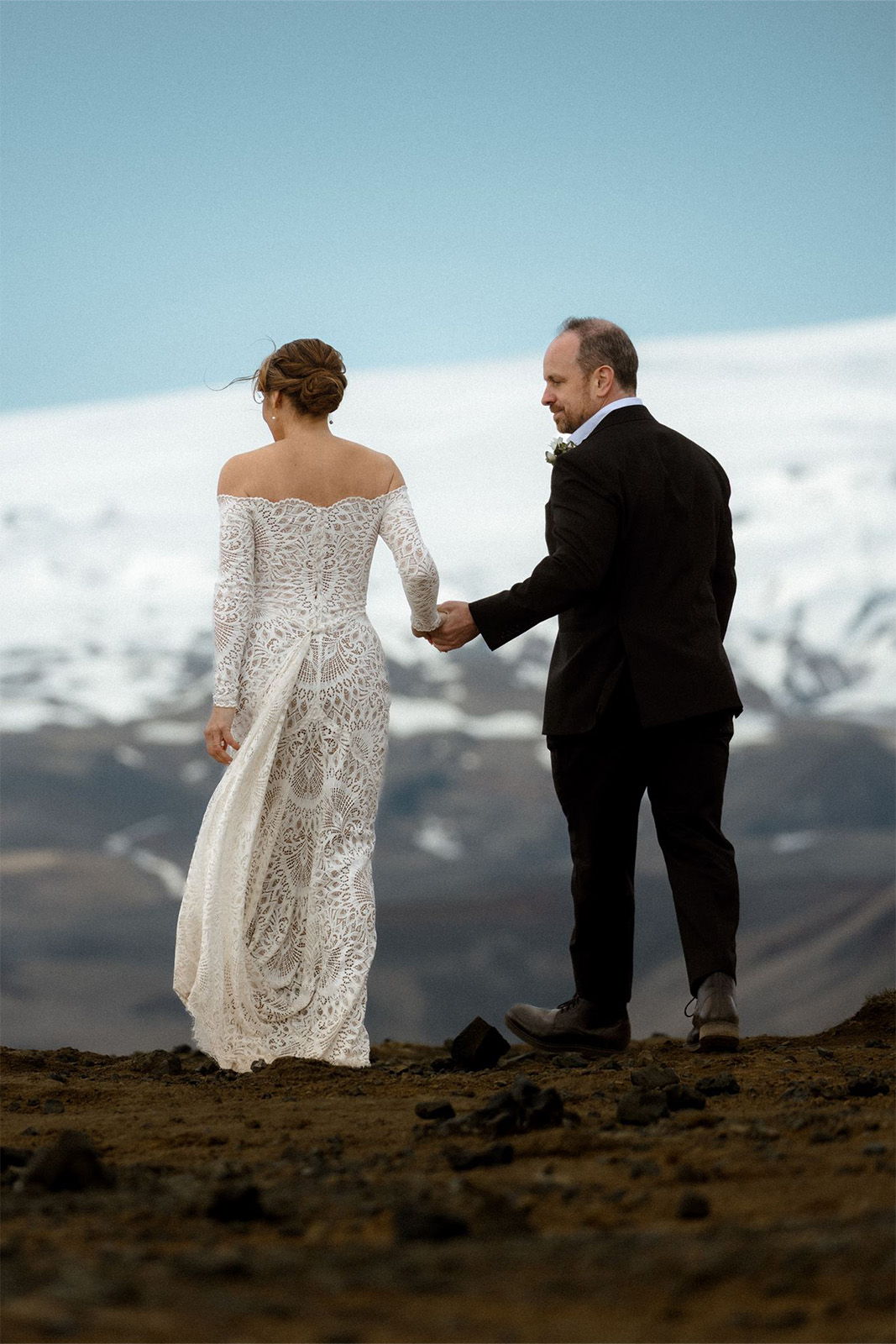 A couple holding hands, dressed for a wedding, with a snowy landscape in the background.