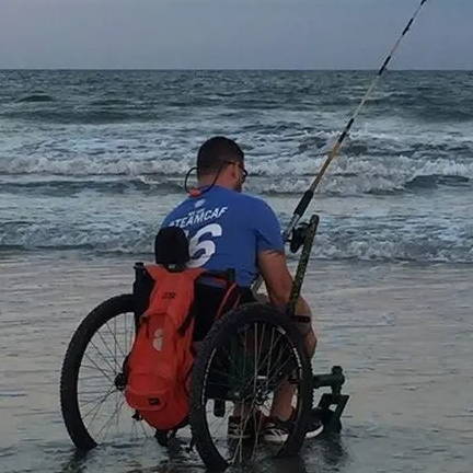 Adult in shallow water and wet sand at coast using GRIT Freedom Chair all terrain wheelchair while fishing in whitewater