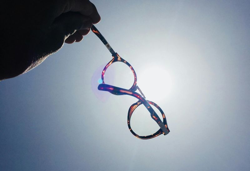 hand holding eyeglasses across bright sunlight in sky