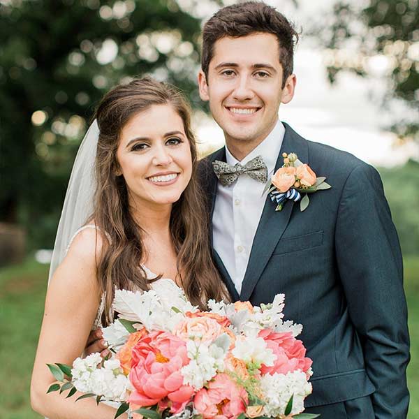 Bride and groom posing outside. Groom wearing a green floral bow tie and bride holding a large bouquet.