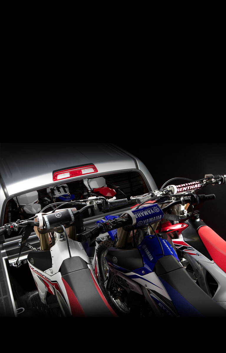 Three dirt bike motorcycles in the cargo bed of a pickup truck.