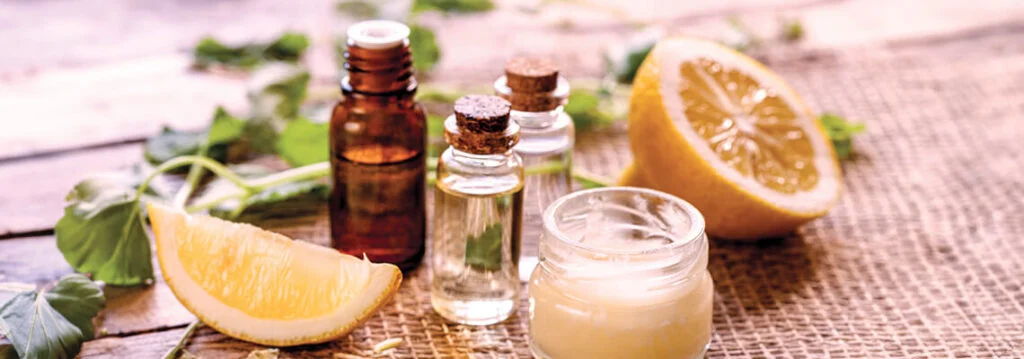 Bottles of essential oils, lemon slices, and cream on a wooden surface.