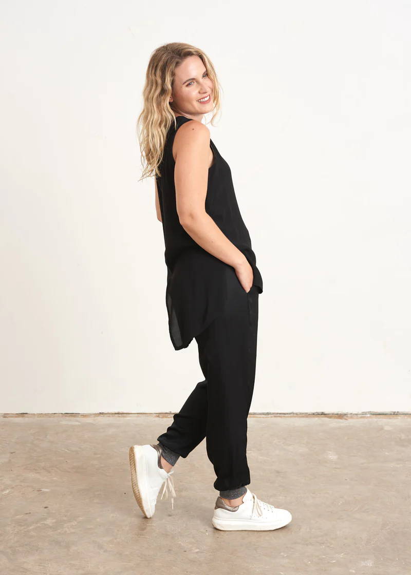 A model wearing a sleeveless black top with a dipped hem with black trousers and white trainers