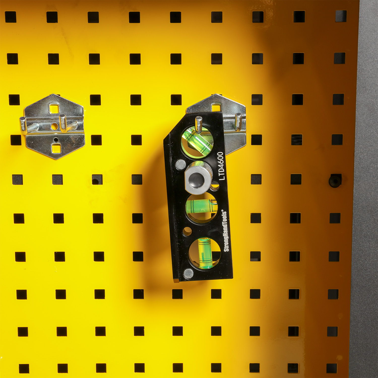 Black spirit level mounted on a yellow pegboard with metal hooks.