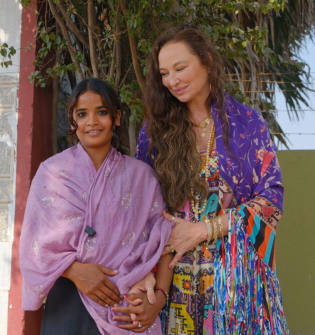 Camilla Franks, Founder and Creative Director, looks down and smiles beside a girl in a lilac shawl from The Butterfly Effect program.