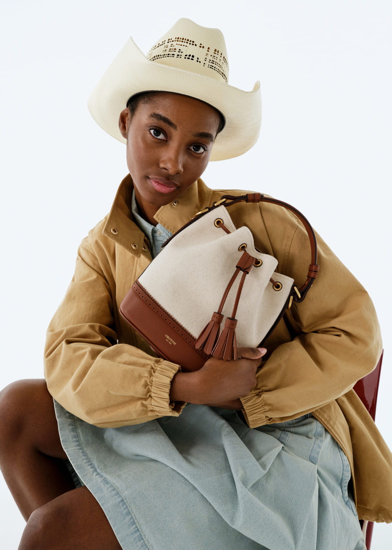 Young woman in cowboy hat holding a stylish bag, sitting elegantly.