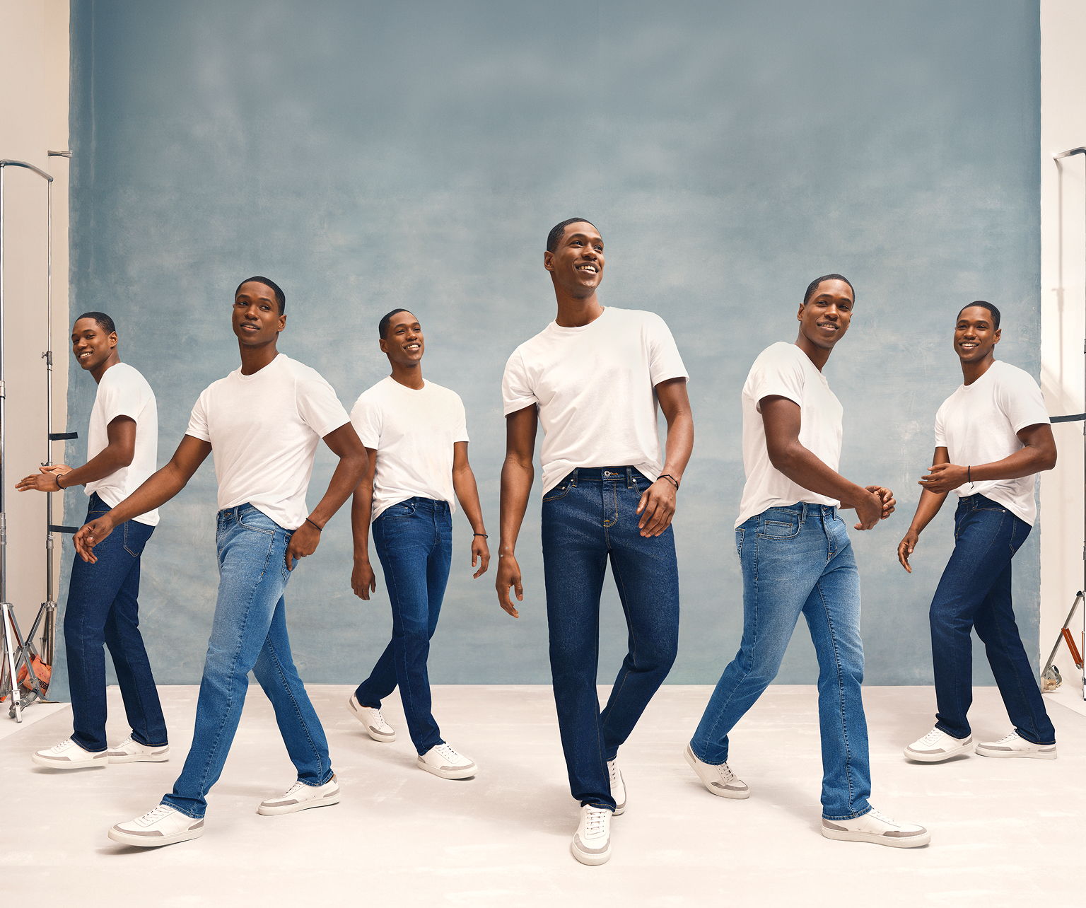 A person in a white shirt and jeans posing in a studio setting.