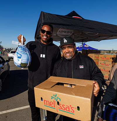 Two men holding food donation items in front of a tent.