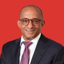 Smiling man in a suit with glasses against a red background.