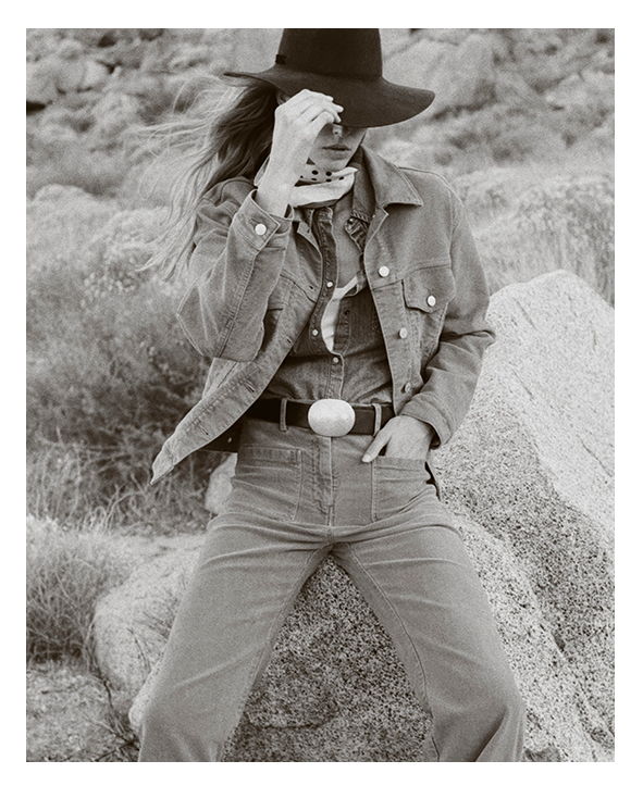 Person in cowboy attire holding a camera, standing on a rock formation.