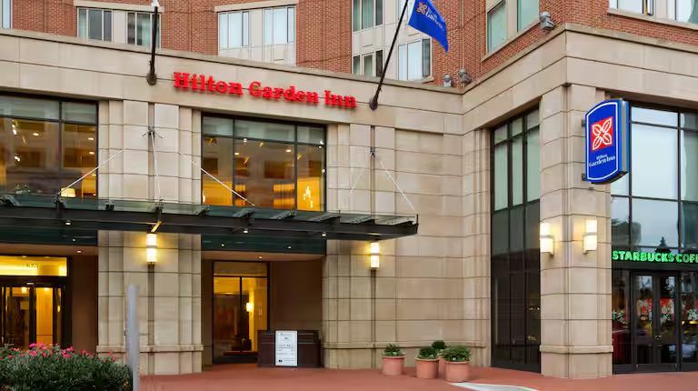 Entrance of the Hilton Garden Inn Baltimore Inner Harbor with red lettering over the front doors, a mid range stay a short walk from Power Plant Live!