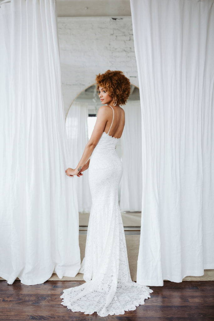La novia lleva el vestido de novia Grace Loves lace Clo entre dos cortinas blancas 