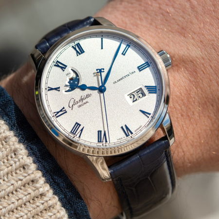 A close-up of a silver watch on a wrist with a blue strap.