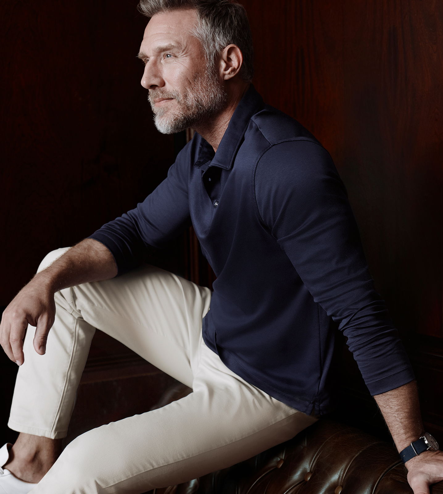 Man sitting on a couch, wearing a navy shirt and cream pants.
