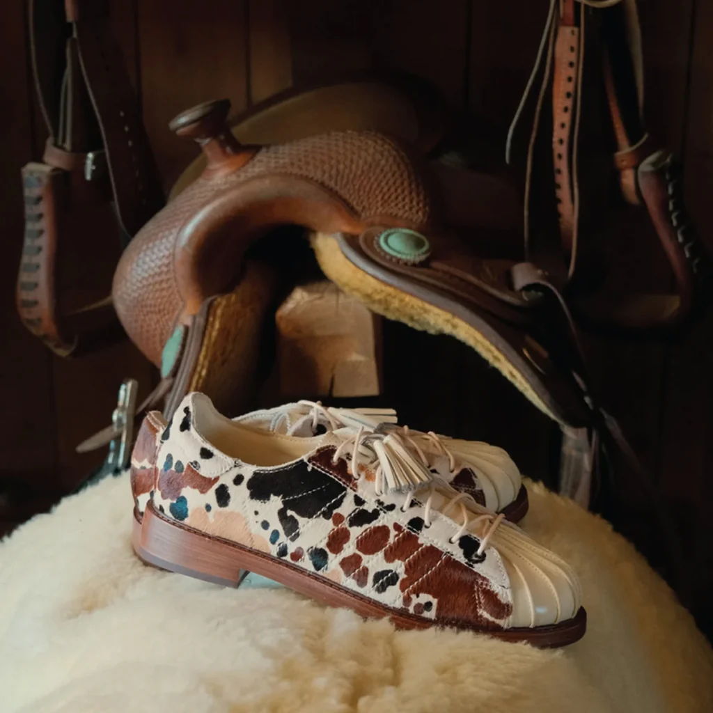 A pair of cow-print shoes next to a saddle.