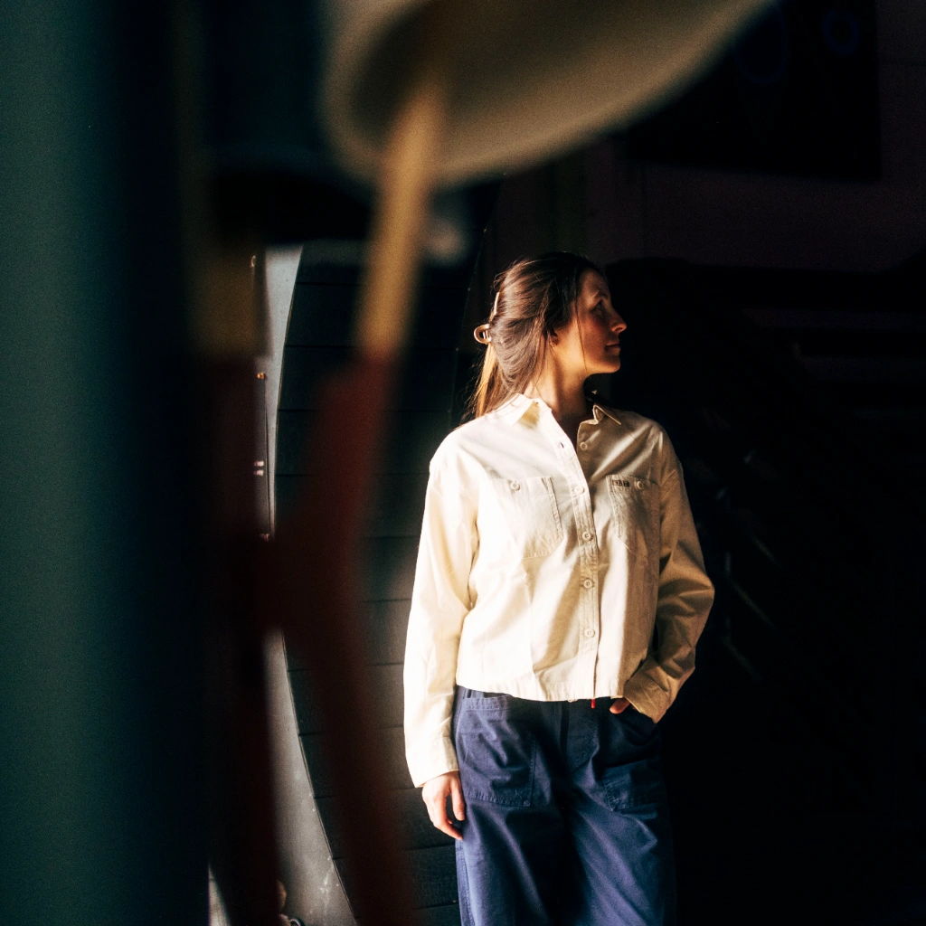 A woman in a white shirt stands in low light.