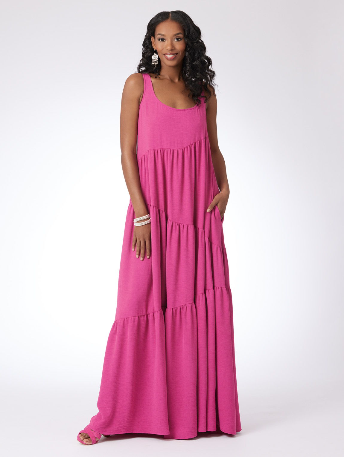 Woman in a pink maxi dress with pockets, standing against a plain background.