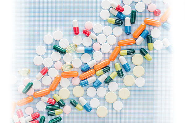Colorful pills and capsules arranged in a wavy pattern on a grid background.