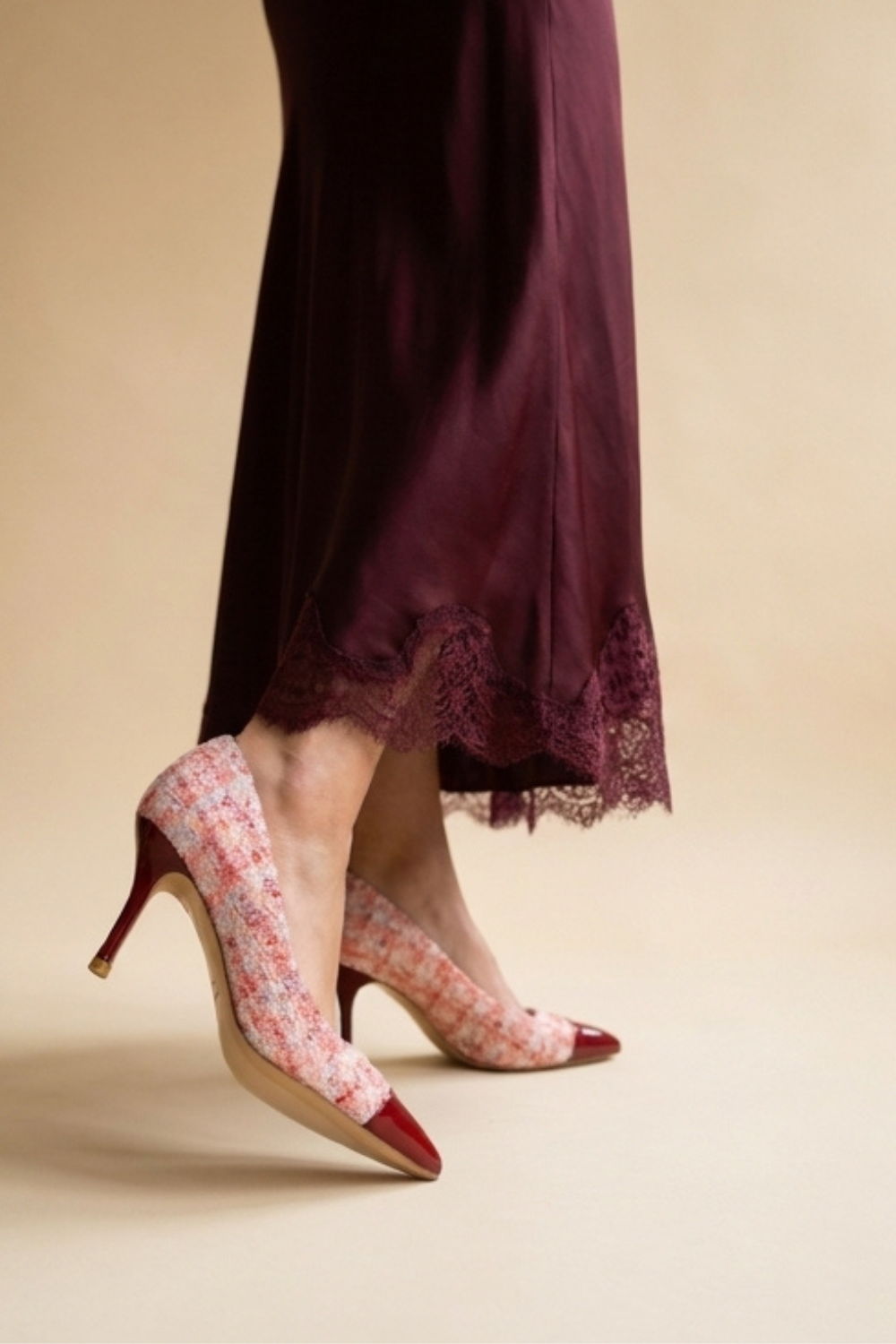 A pair of stylish high heels worn with a flowing burgundy dress.
