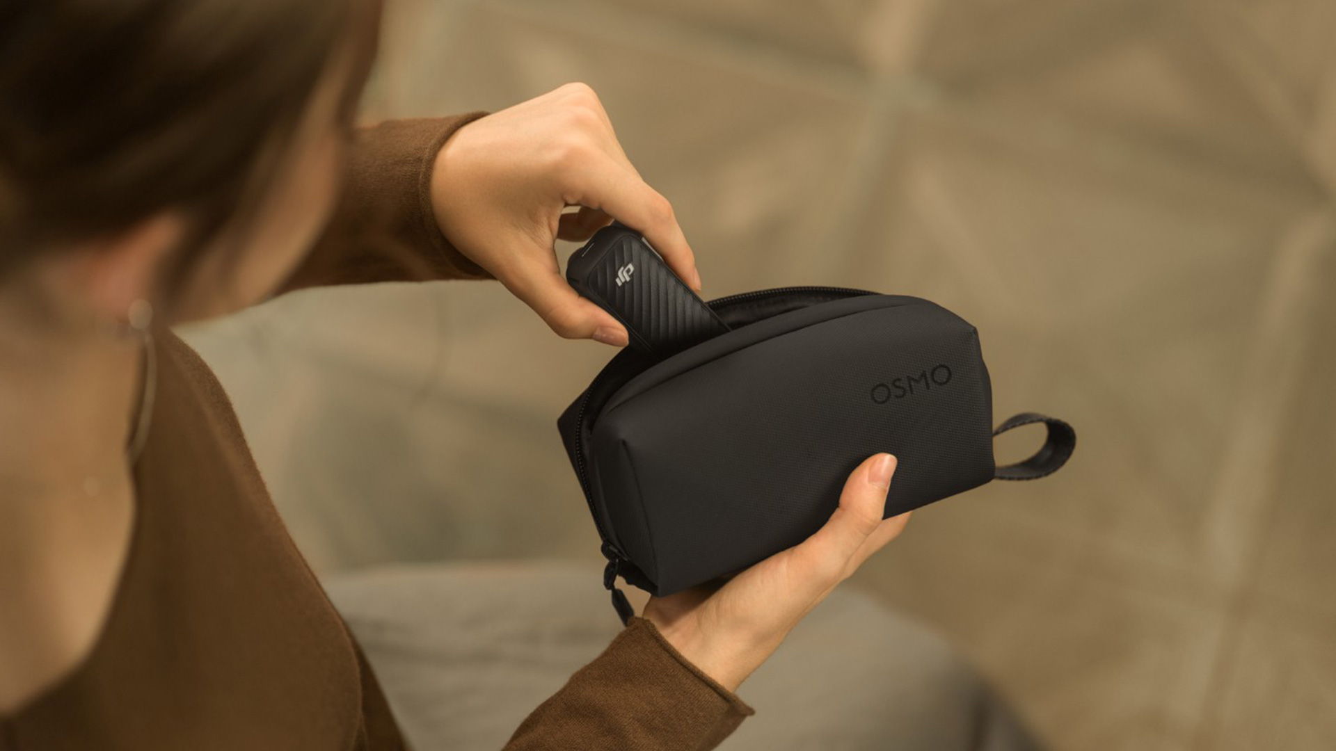 A person putting a DJI Osmo Pocket 4 into a black carrying bag.